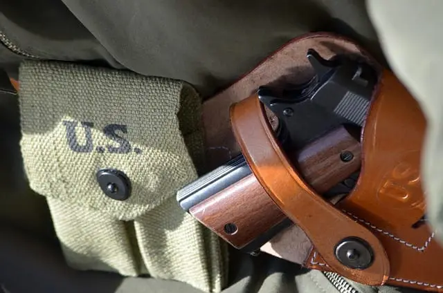 Pistola con guancette in legno in una fondina di cuoio marrone, accanto a una giberna militare in tela verde