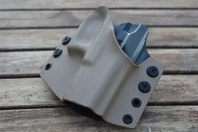 Fondina in kydex color sabbia con una pistola, appoggiata su un tavolo di legno
